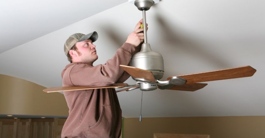A master electrician installing a ceiling fan in a residential room.