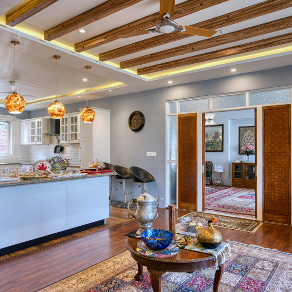 Open-plan living and kitchen area with pendant lights, wooden ceiling beams, modern furniture, decorative rugs on wooden flooring, and space designed to accommodate recessed lighting installation.