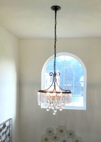 An elegant chandelier hangs over a bedroom window, expertly installed by a master electrician.