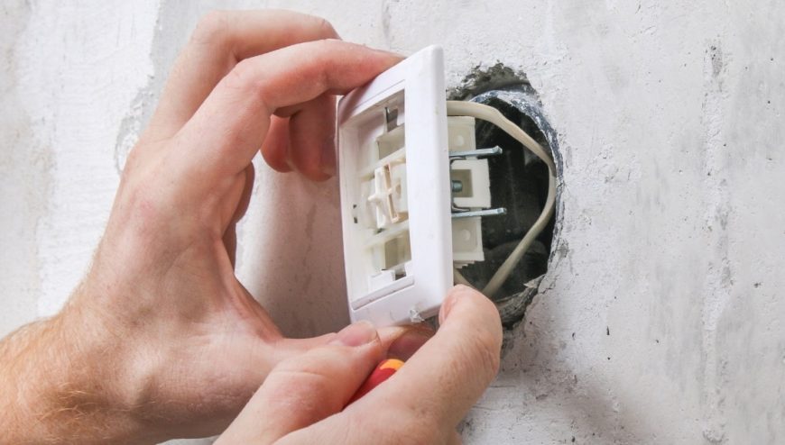 A residential electrician installing a light switch on a wall.