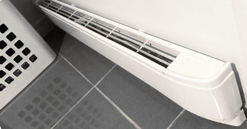 A white radiator, installed by a residential electrician, sitting on a tiled floor.
