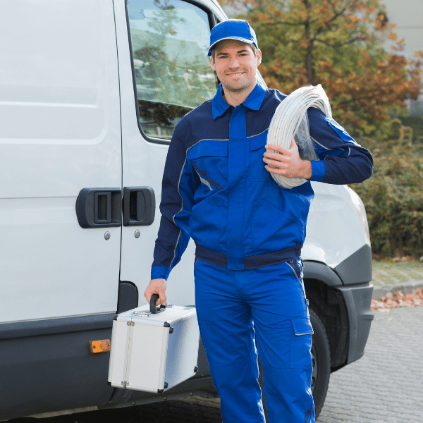 A man in a blue uniform stands by a white van, holding a coil of cable over his shoulder and carrying a metal toolbox—ready for whole home generator installation.