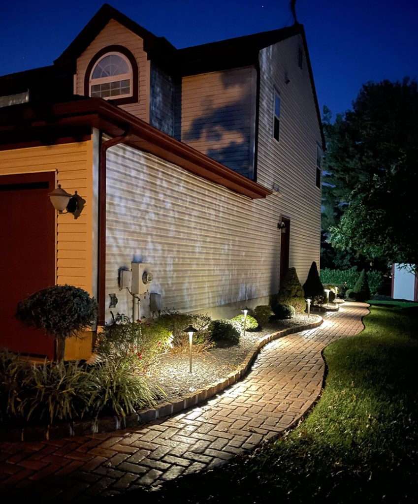 A residential walkway illuminated at night in front of a house.